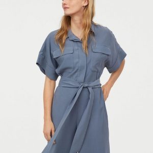 Woman wearing a light blue utility jumpsuit with short sleeves and a belt at the waist.