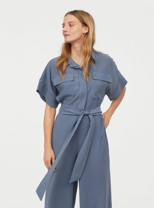 Woman wearing a light blue utility jumpsuit with short sleeves and a belt at the waist.