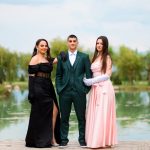 Group of three individuals in formal attire posing by a serene water body, showcasing elegant dresses and a suit, perfect for event photography.