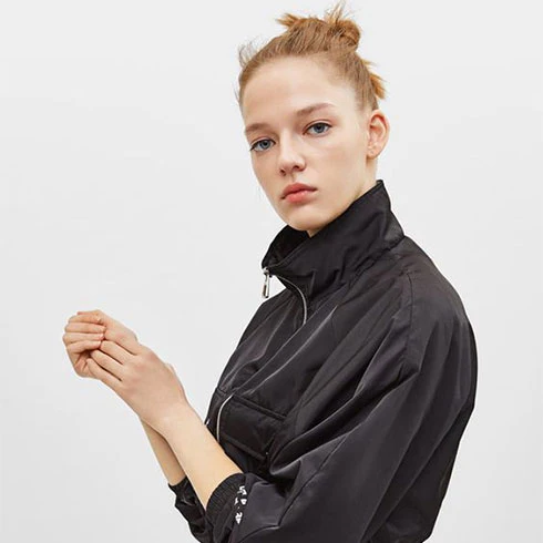 Model wearing a black zip-up jacket with a high collar, showcasing a minimalist style and modern design, suitable for casual wear.